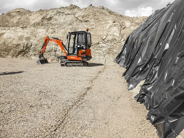 Bagger beim Bodenaushub neben Kieshaufen